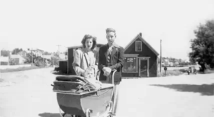 Couple standing behind a baby carriage in the 1950s with a baby looking out from the carriage
