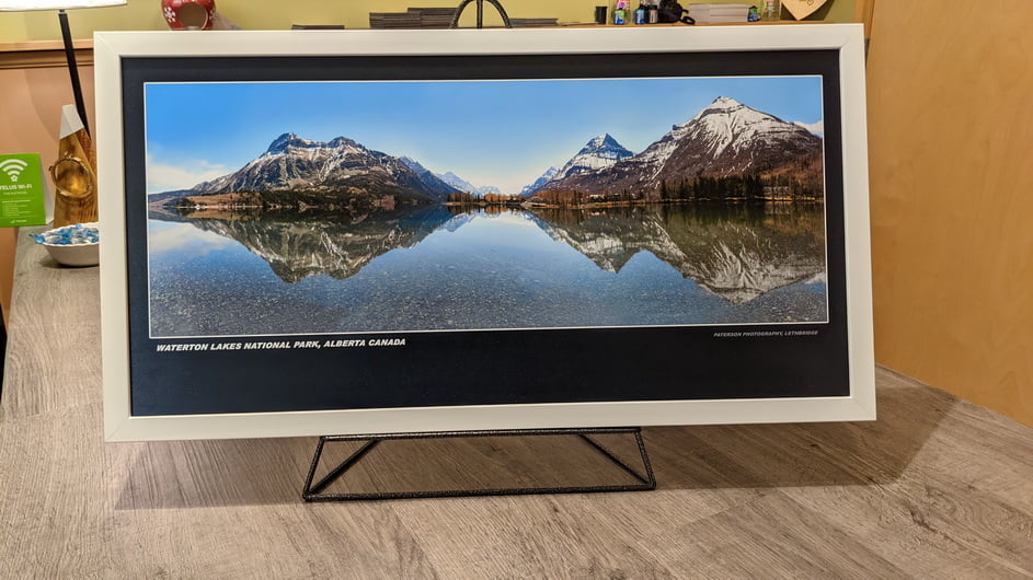 White picture frame with a mounted and laminated print of Waterton Lakes National park with calm water and the mountains